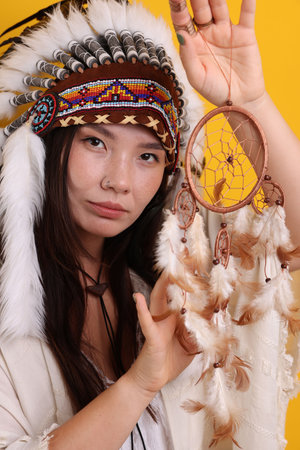 Shaman woman in native American Indian headdress with dreamcatcher on orange backgroundの写真素材