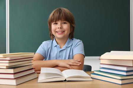Back to school. Boy with books at wooden desk against chalkboard indoorsの写真素材