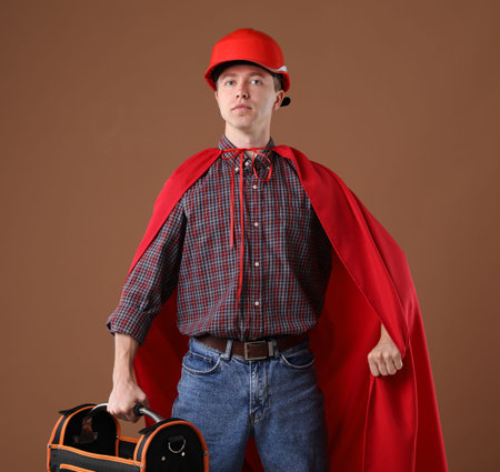 Builder with toolbox wearing hardhat and superhero cape on brown backgroundの写真素材