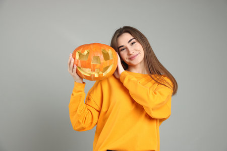 Happy Halloween. Woman with carved Jack-o'-lantern pumpkin on gray backgroundの写真素材