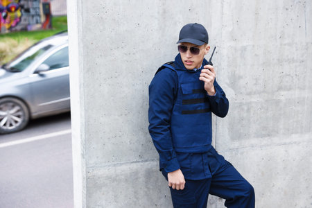 Police officer talking on radio near wall outdoors. Space for text