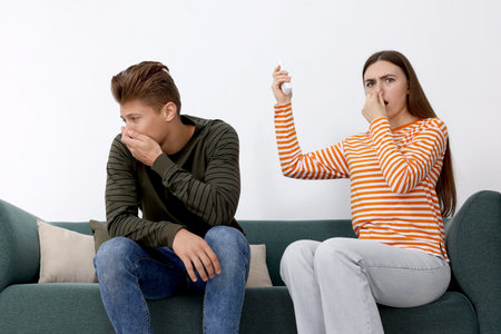 Unhappy couple with remote control suffering from bad smell and covering their noses indoorsの写真素材