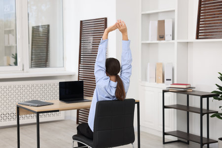 Young businesswoman stretching at table in office, back viewの写真素材
