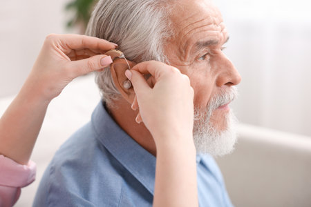 Caregiver helping senior man to put in hearing aid at home, closeupの写真素材
