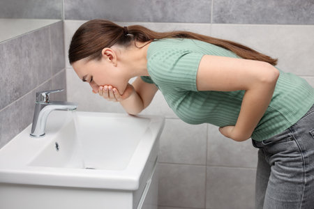 Woman suffering from stomach ache and nausea over sink in bathroomの写真素材