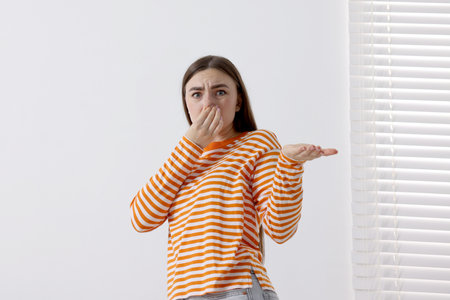 Young woman suffering from smell and covering her nose indoorsの写真素材