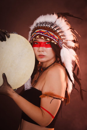 Shaman woman in native American headdress with tambourine on dark backgroundの写真素材