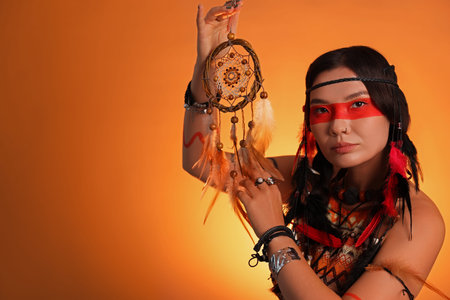 Shaman woman with face painting and dreamcatcher on orange gradient background, space for textの写真素材