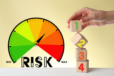Scale with arrow indicating level of risk against beige background. Woman taking cube with green 1 as low level of risk, closeupの写真素材