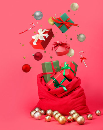 Christmas balls, gift boxes, candy canes and confetti falling into bag on pink backgroundの写真素材