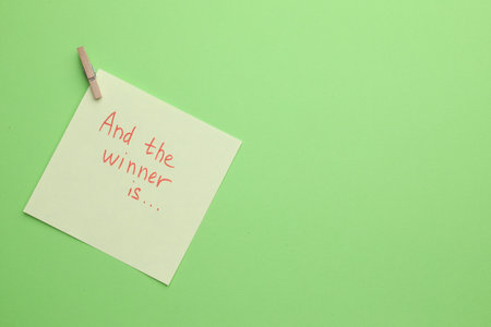 Sticky note with phrase And The Winner Is on green background, top view. Space for textの写真素材