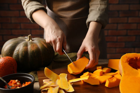 Woman cutting pumpkin at table against brick wall, closeupの写真素材