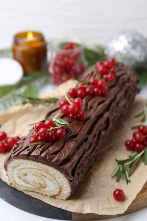 Delicious Yule log (traditional Christmas cake) with redcurrant on white table, closeupの写真素材