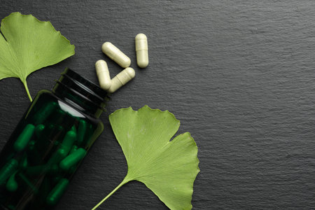 Ginkgo biloba leaves and medical bottle with pills on dark textured table, flat lay. Space for textの写真素材