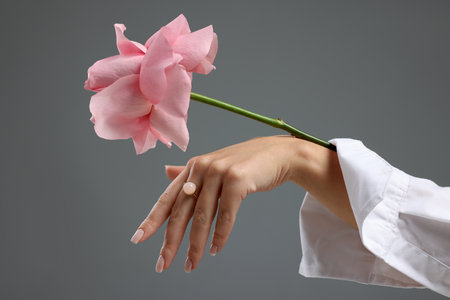 Woman with beautiful flower wearing stylish ring on gray background, closeupの写真素材