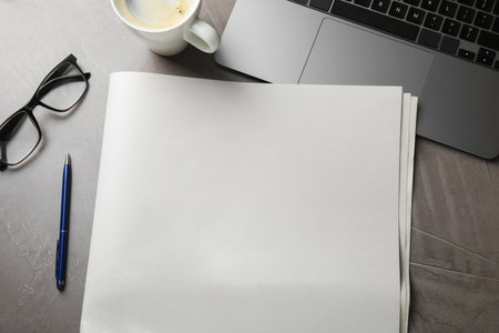 Newspaper, coffee, pen, laptop and glasses on gray table, flat lay. Mockup for designの写真素材