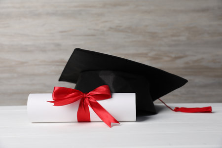 Graduation hat and diploma on white wooden tableの写真素材