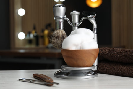 Metal stand with shaving brush, razors and bowl of foam on light wooden table in barbershop, closeupの写真素材
