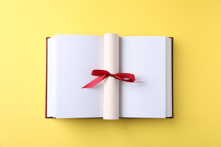 Diploma and book on yellow background, top viewの写真素材