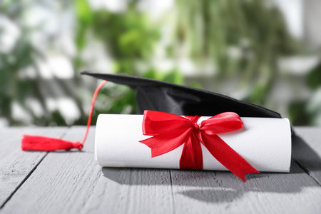 Diploma and graduation hat on gray wooden table outdoors, closeupの写真素材