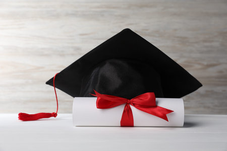Graduation hat and diploma on white wooden tableの写真素材