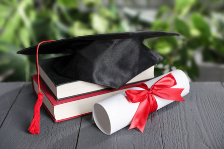 Diploma, graduation hat and books on gray wooden table outdoors, closeupの写真素材