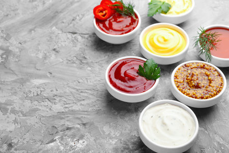 Different sauces in bowls and ingredients on gray textured table, closeup. Space for text
