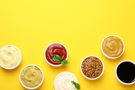 Different sauces and herbs on yellow background, flat lay. Space for textの写真素材