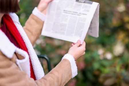 Woman in coat reading newspaper outdoors, closeup