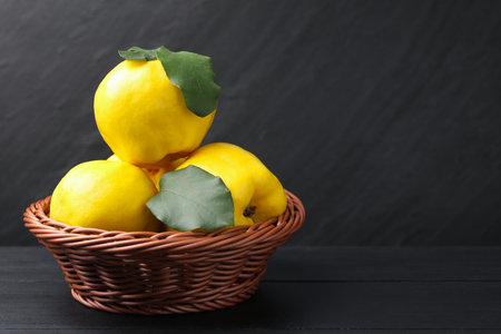 Ripe quinces with green leaves in wicker basket on black wooden table, closeup. Space for textの写真素材