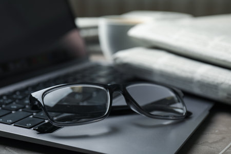 Laptop, glasses and newspapers on gray table, closeupの写真素材