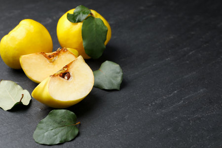 Ripe quinces and green leaves on black textured table, closeup. Space for textの写真素材