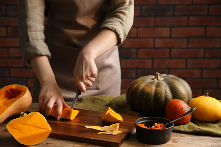 Woman cutting pumpkin at wooden table against brick wall, closeupの写真素材