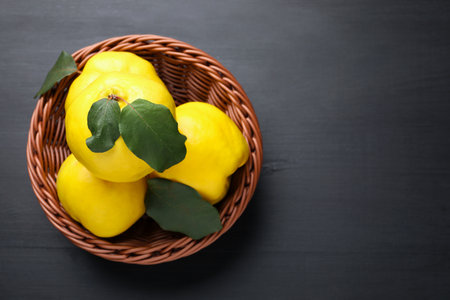 Ripe quinces with green leaves in wicker basket on black wooden table, top view. Space for textの写真素材