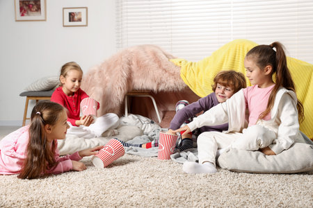 Cute children in pajamas with popcorn on floor at homeの写真素材