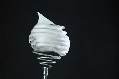 Whisk with whipped egg whites on black background. Space for textの写真素材