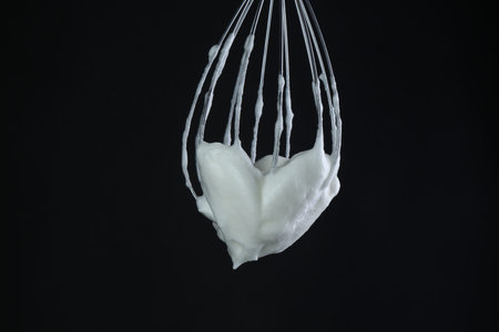 Whisk with whipped egg whites on black backgroundの写真素材