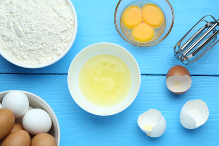 Broken eggs, mixer and products on blue wooden table, flat layの写真素材