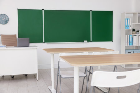 Green chalkboard, desks and chairs in classroom. Mockup for designの写真素材