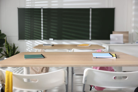 Green chalkboard, desks and chairs with backpacks in classroom