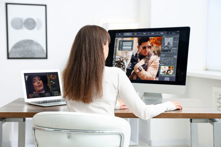 Professional retoucher editing photo on computer and laptop at table in office, back view