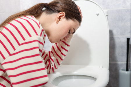 Woman suffering from nausea over toilet bowl in bathroomの写真素材