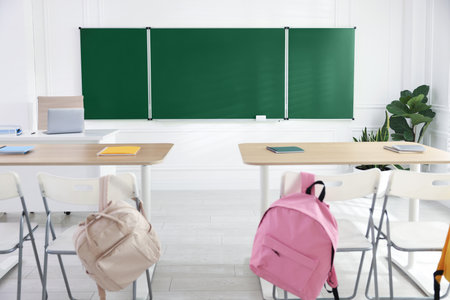 Green chalkboard, backpacks and stylish furniture in classroom. Mockup for designの写真素材