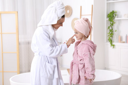 Mother applying cream on her daughter's face in bathroomの写真素材