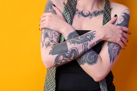 Young woman with tattoos and stylish clothes posing on yellow background, closeupの写真素材