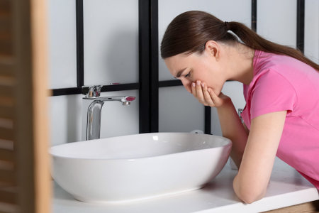Woman suffering from nausea over sink in bathroomの写真素材