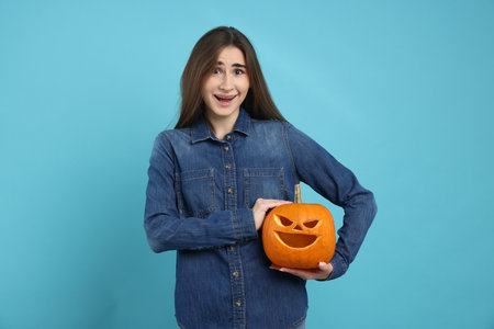 Happy Halloween. Woman with carved Jack-o'-lantern pumpkin on light blue backgroundの写真素材