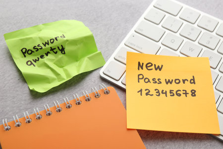 Changing password. Sticky notes with old and new passcodes, computer keyboard and notebook on gray table, closeupの写真素材