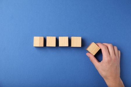 Hand with wooden cubes on blue background, top view