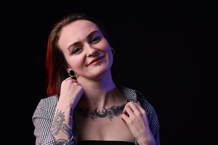 Young woman with piercings, tattoos and stylish clothes on black background, space for textの写真素材